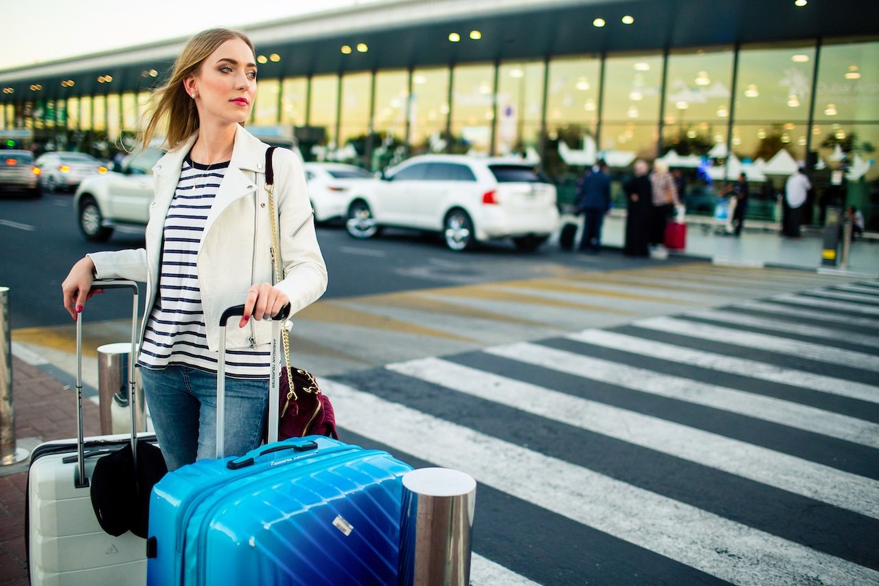 stunning blonde lady with blue white suitcases stands before crossing street